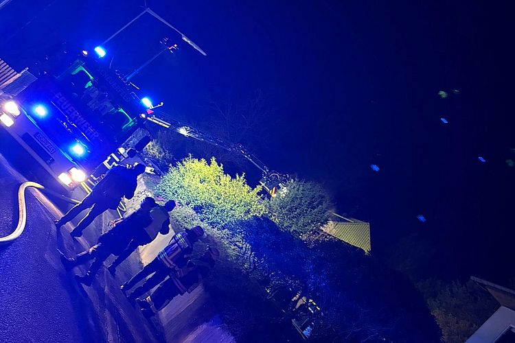 Foto zum Einsatzbericht: 022026 Dachstuhlbrand in Scheuerfeld, abgebildet sind Einsatzkräfte der Feuerwehr und DRK, sowie ein Fahrzeug der Feuerwehr