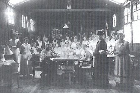 Bahnhofsmission_im_Ersten_Weltkrieg Versammelt um einen Tisch Helferinnen des vaterländischen Frauenvereins und der Sanitätskollone in einen Bahnhofsnebengebäude.