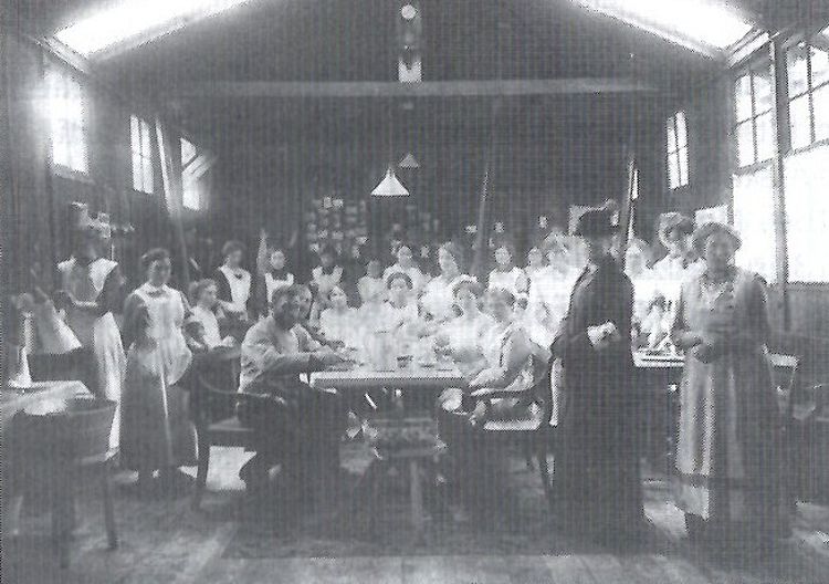 Versammelt um einen Tisch Helferinnen des vaterländischen Frauenvereins und der Sanitätskollone in einen Bahnhofsnebengebäude.