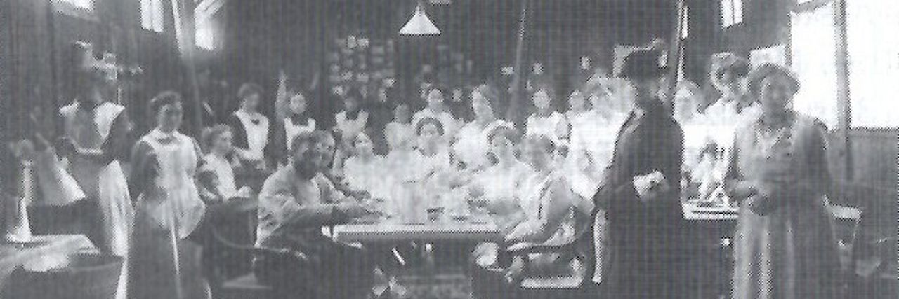 Versammelt um einen Tisch Helferinnen des vaterländischen Frauenvereins und der Sanitätskollone in einen Bahnhofsnebengebäude.