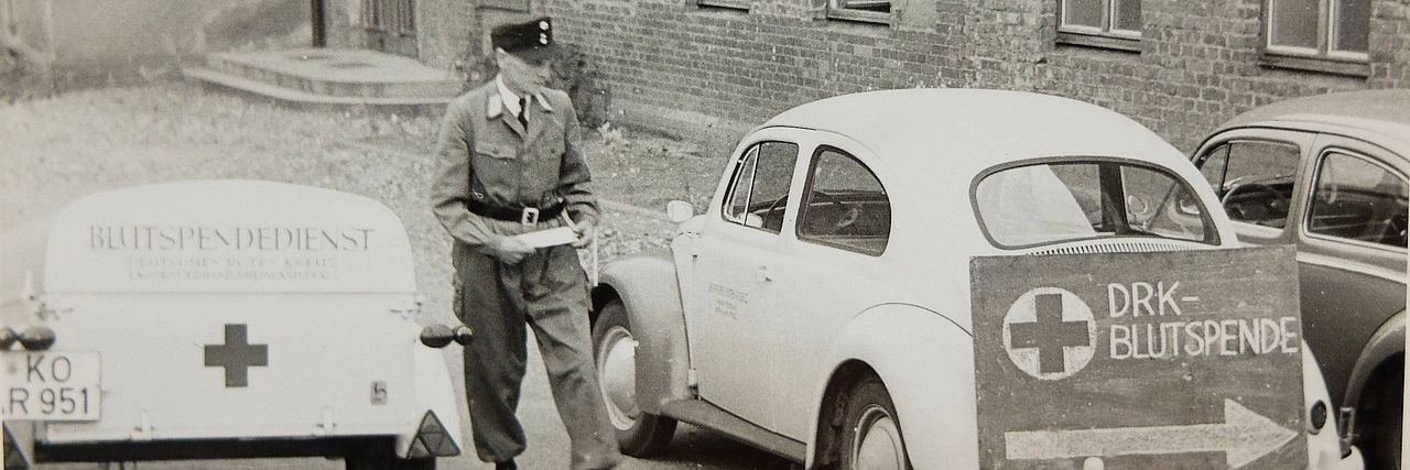 1958 Erster Blutspendetermin im Kreisverband in der Berufsschule Wissen, Käfer und Blutspende-Hinweisschilder.
