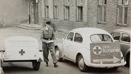 1958 Erster Blutspendetermin im Kreisverband in der Berufsschule Wissen, Käfer und Blutspende-Hinweisschilder.