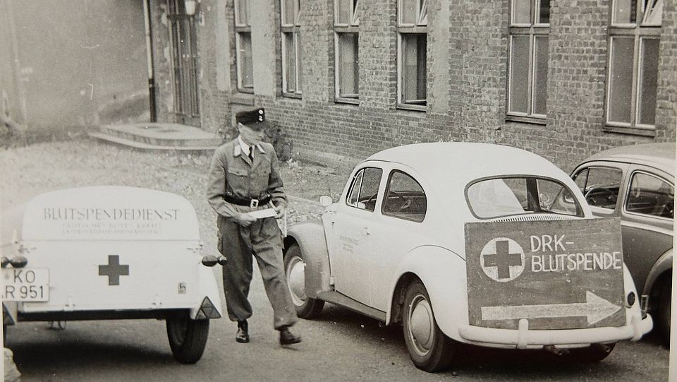 1958 Erster Blutspendetermin im Kreisverband in der Berufsschule Wissen, Käfer und Blutspende-Hinweisschilder.