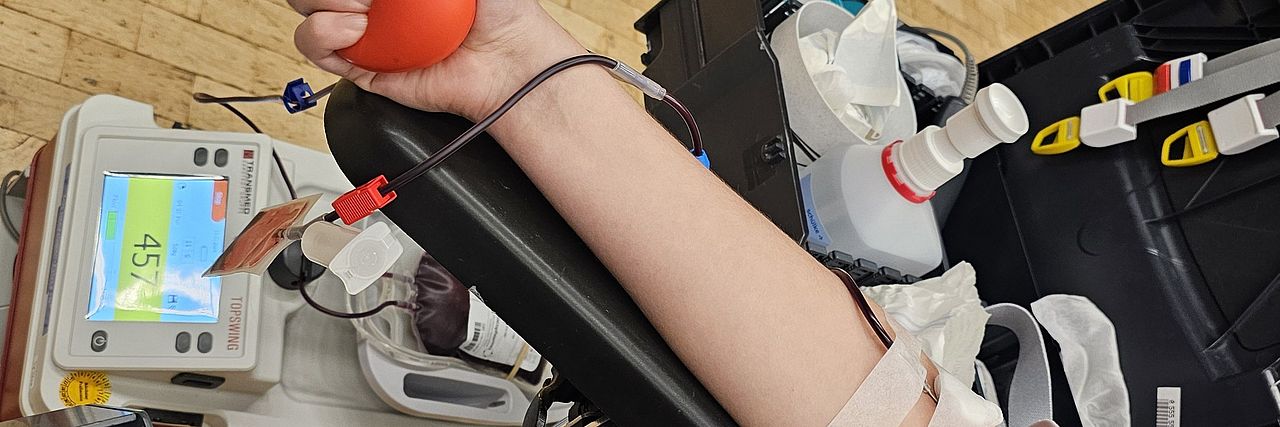 Abgebildet ist der Arm einer Helferin, während der Blutspende.