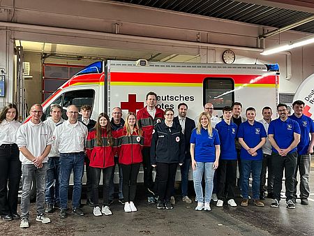 Gruppenfoto der Mitgliederversammlung des Ortsvereins 2025. Im Hintergrund RTW und Beachflag.